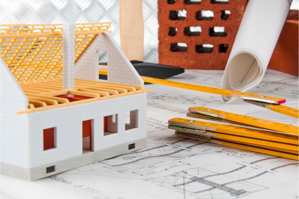 grafika z mini konstrukcją domu, oraz planem budowlanym w tle