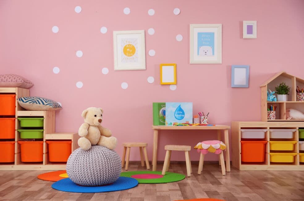 pokój dziecięcy w kolorze różowym z drewnianymi meblami i kolorowymi dodatkami