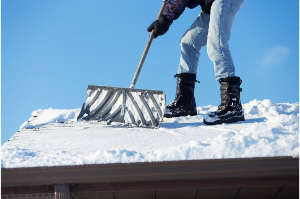 mężczyzna odgarniający łopatą śnieg z dachu