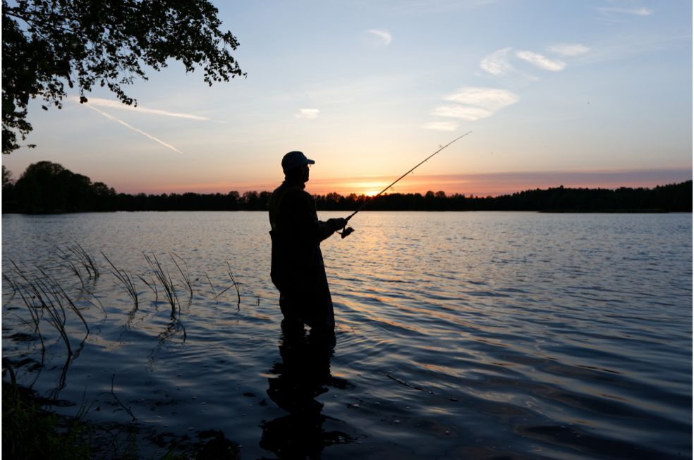 wędkarz łowiący ryby w jeziorze podczas zachodu słońca