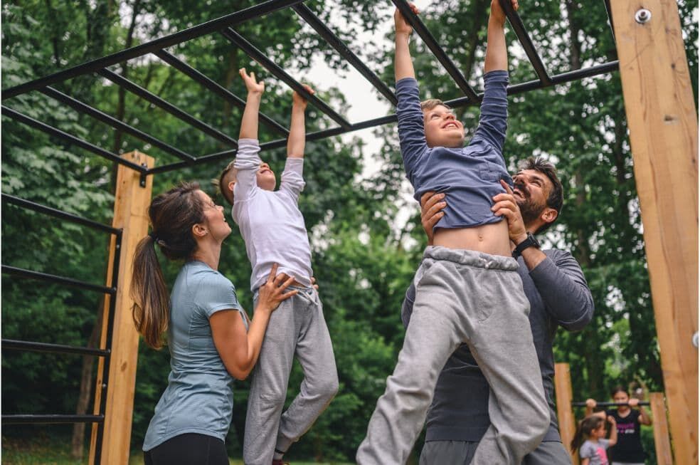 dzieci z rodzicami bawiące się na plenerowej siłowni