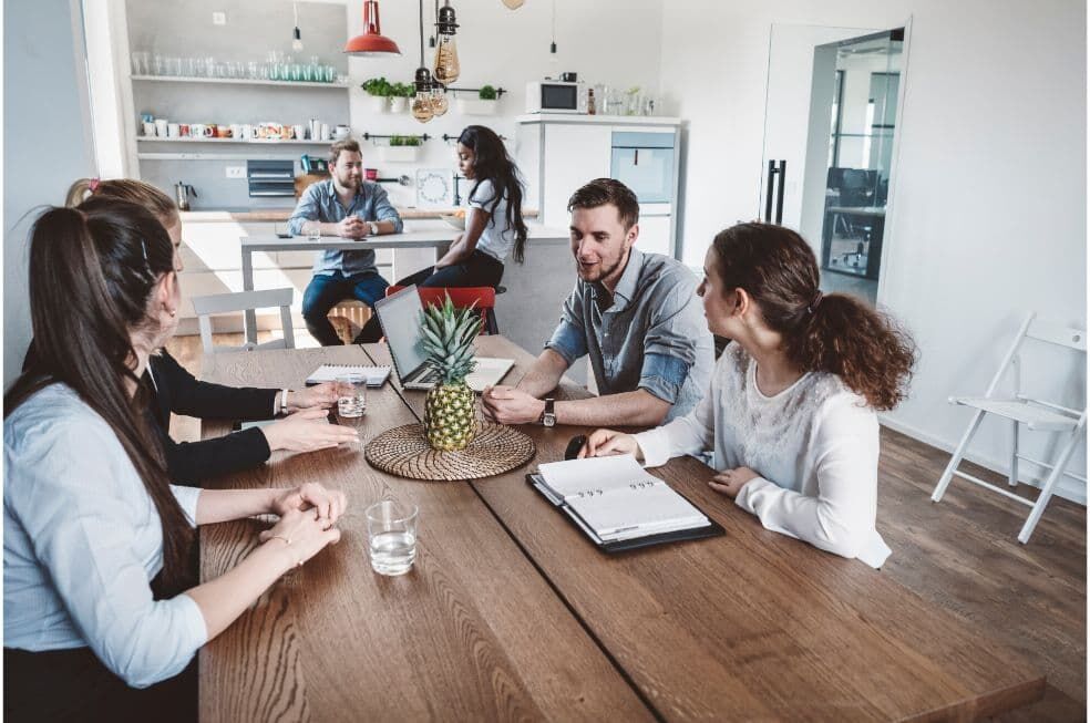 pracownicy w biurowej kuchni rozmawiają przy jednym stole